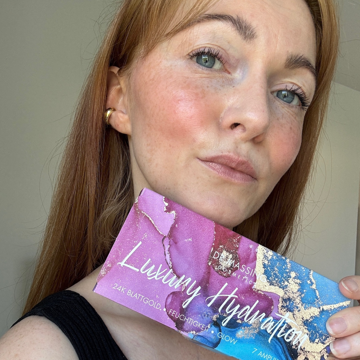 Frau hält Luxury Hydration Ampullen Box in der Hand neben ihr Gesicht und schaut in die Kamera
