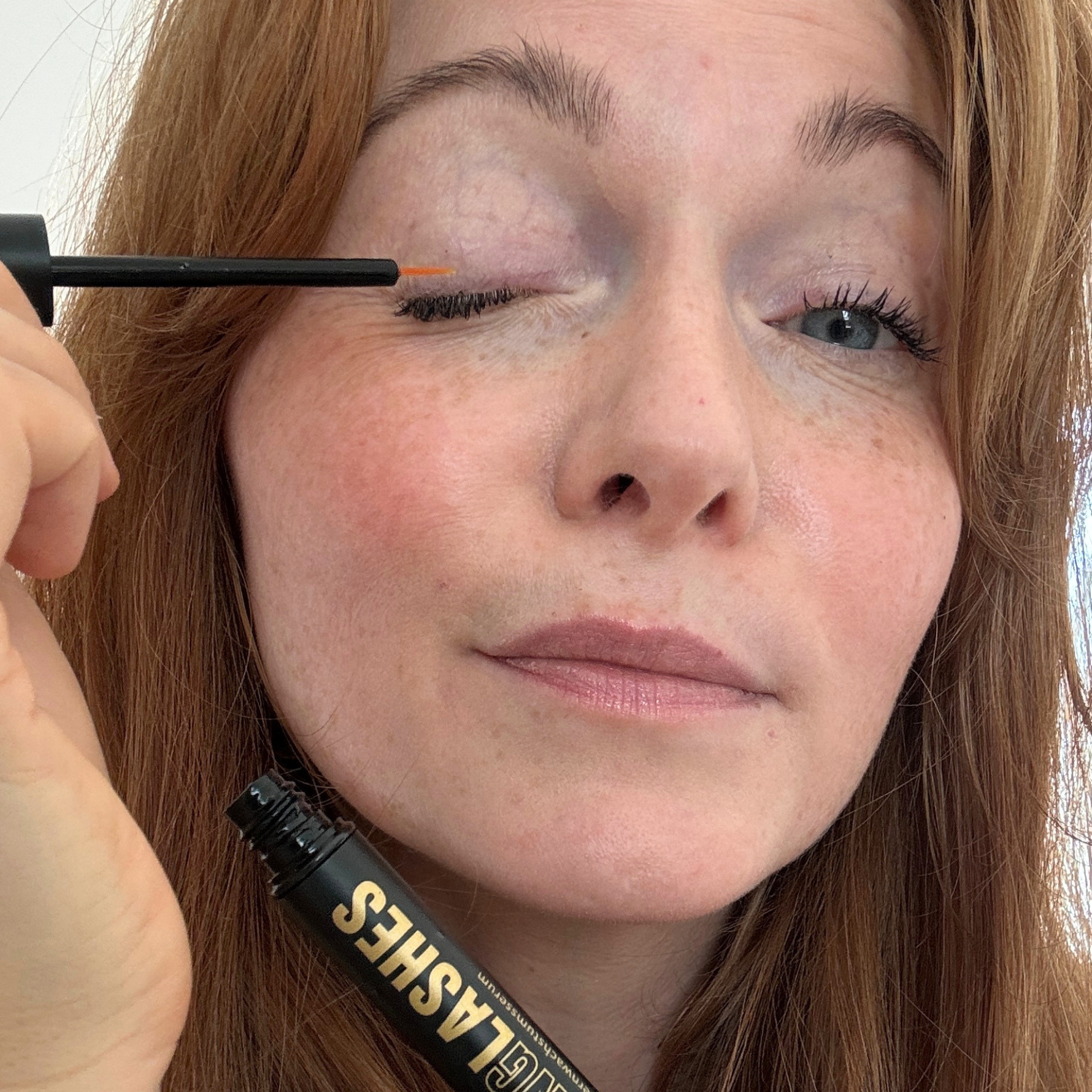 Junge Frau trägt Sensitive Wimpernserum mit Applikator am Wimpernkranz auf