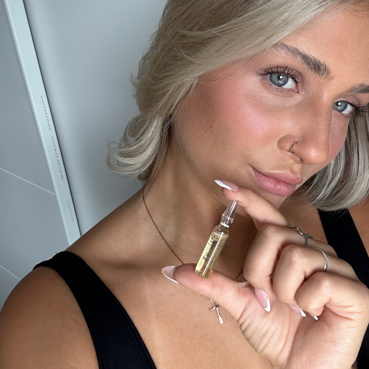 Frau hält Skin Repair Ampulle in der Hand neben ihr Gesicht und schaut in die Kamera