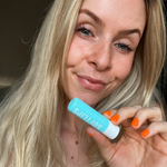 Frau hält Dr. Massing SoftLips Lippenpflege Petrol in der Hand neben ihr Gesicht und schaut in die Kamera