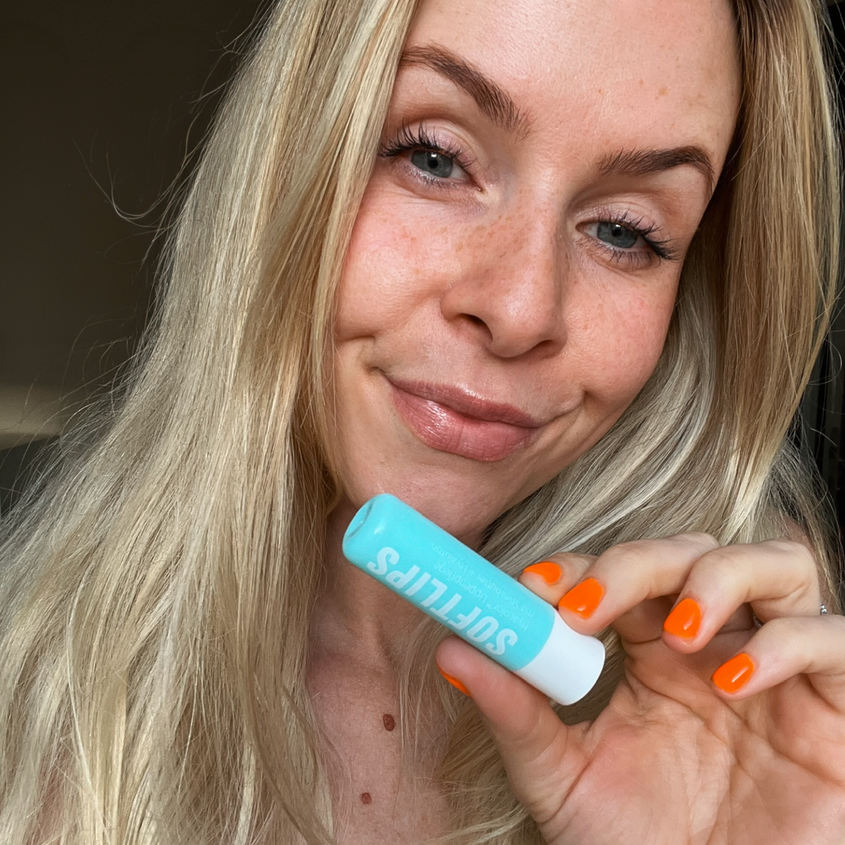 Frau hält Dr. Massing SoftLips Lippenpflege Petrol in der Hand neben ihr Gesicht und schaut in die Kamera