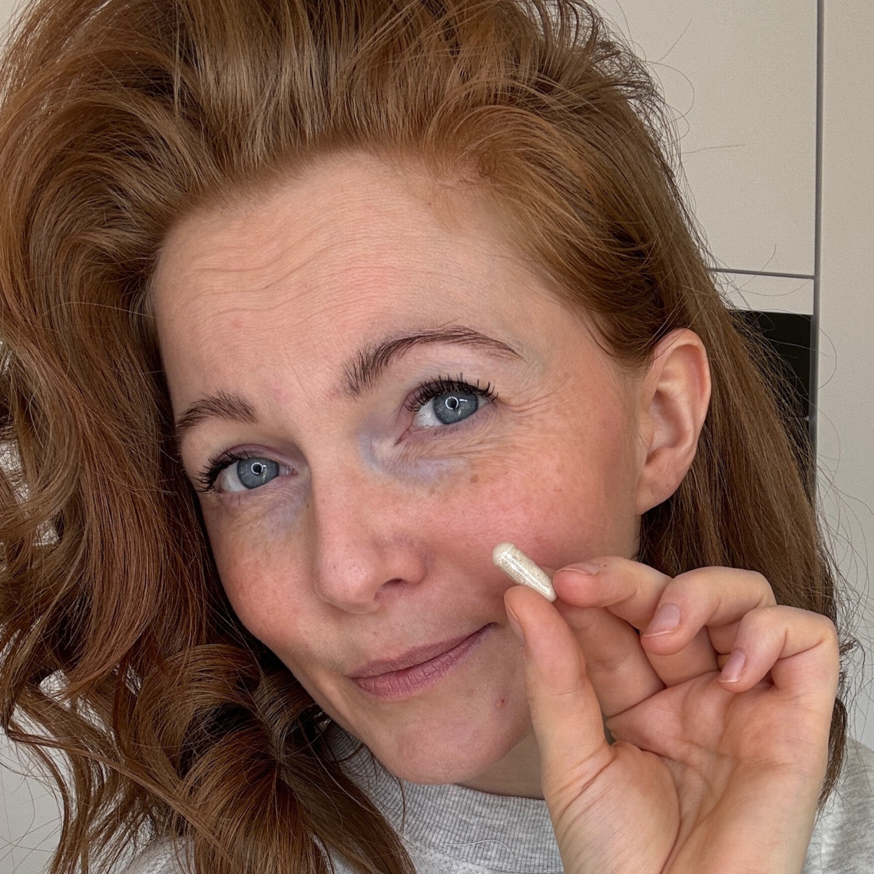 Eine junge Frau hält eine Full Hair Kapsel in die Kamera und lächelt