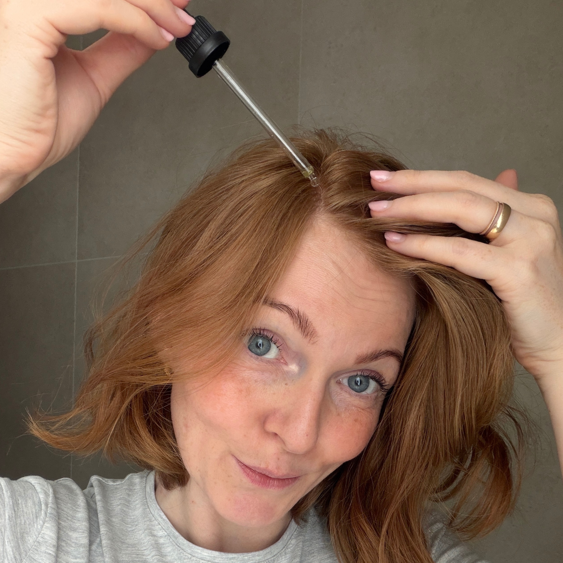 Eine junge Frau trägt mit einer Pipette das Full Hair Haarserum auf die Kopfhaut auf
