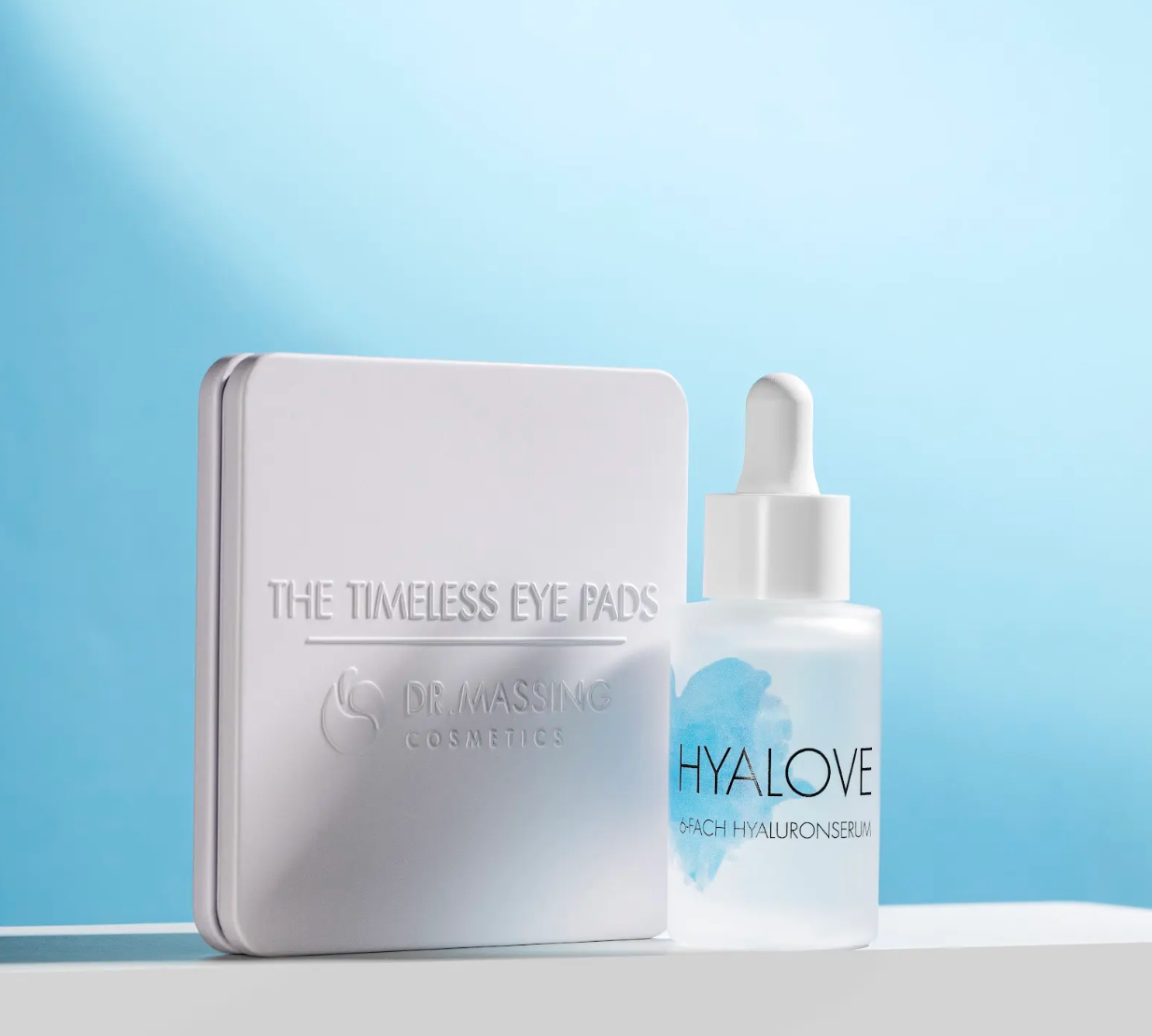 Hyalove Serum und Augenpads in weißer Box stehen vor blauem Hintergrund auf einem weißen Podest