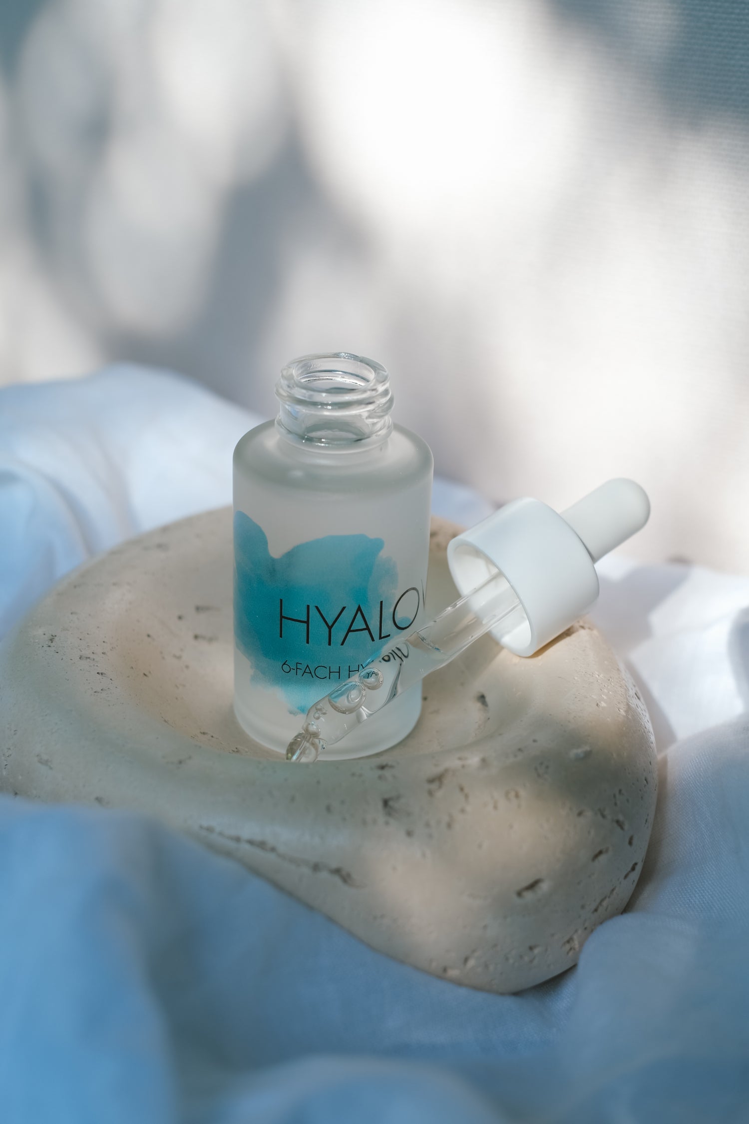 Produktbild von Hyalove Hyaluronserum auf einem beigen Teller und weißem Bettlaken und Sonnenlicht Einstrahlung