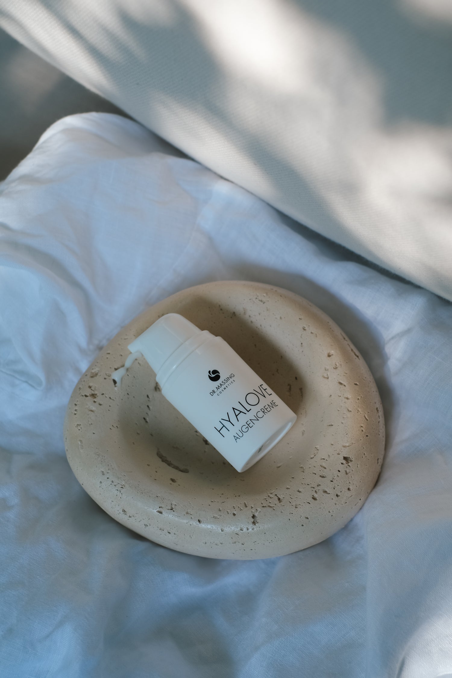 Produktbild von Hyalove Augencreme auf einem beigen Teller und weißem Bettlaken und Sonnenlicht Einstrahlung