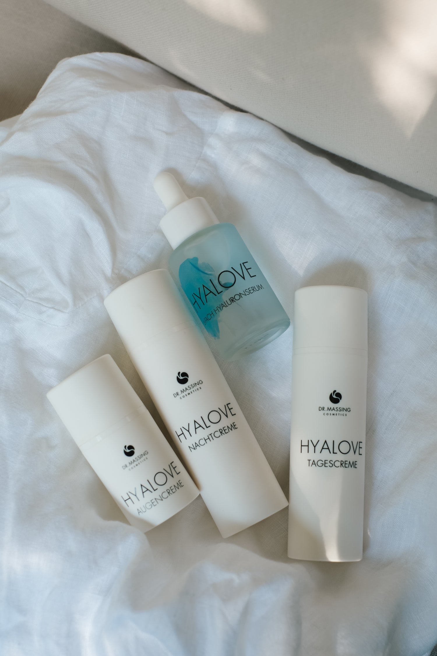 Produktbild von Hyalove Glass Skin Set liegend auf einem weißem Bettlaken mit Hyaluronserum, Tagescreme, Augencreme und Nachtcreme