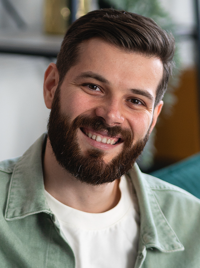 Portrait eines jungen Mannes mit Bart und vollem Haar, lächelt freundlich in die Kamera