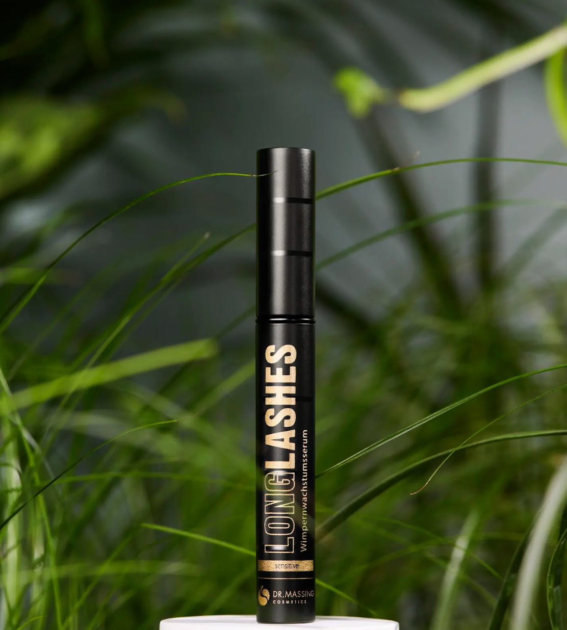 Dr. Massing Sensitive Serum Produkt steht auf weißem Podest vor grünen Pflanzen im Hintergrund