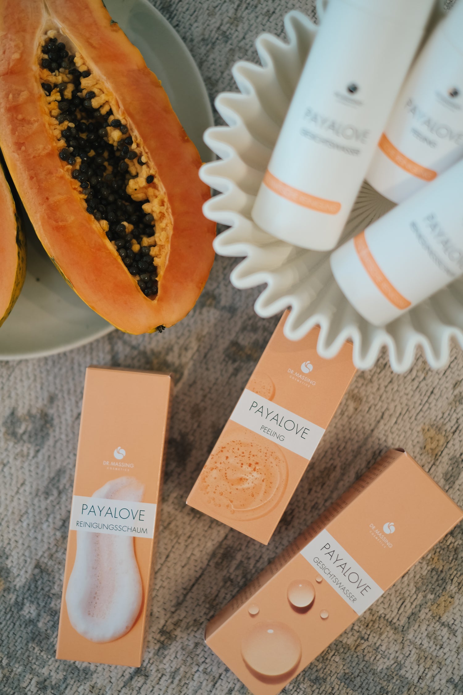Payalove 3er Set mit Gesichtsreiniger, Gesichtswasser und Peeling liegen in beiger Schale neben Papaya und Produktverpackungen