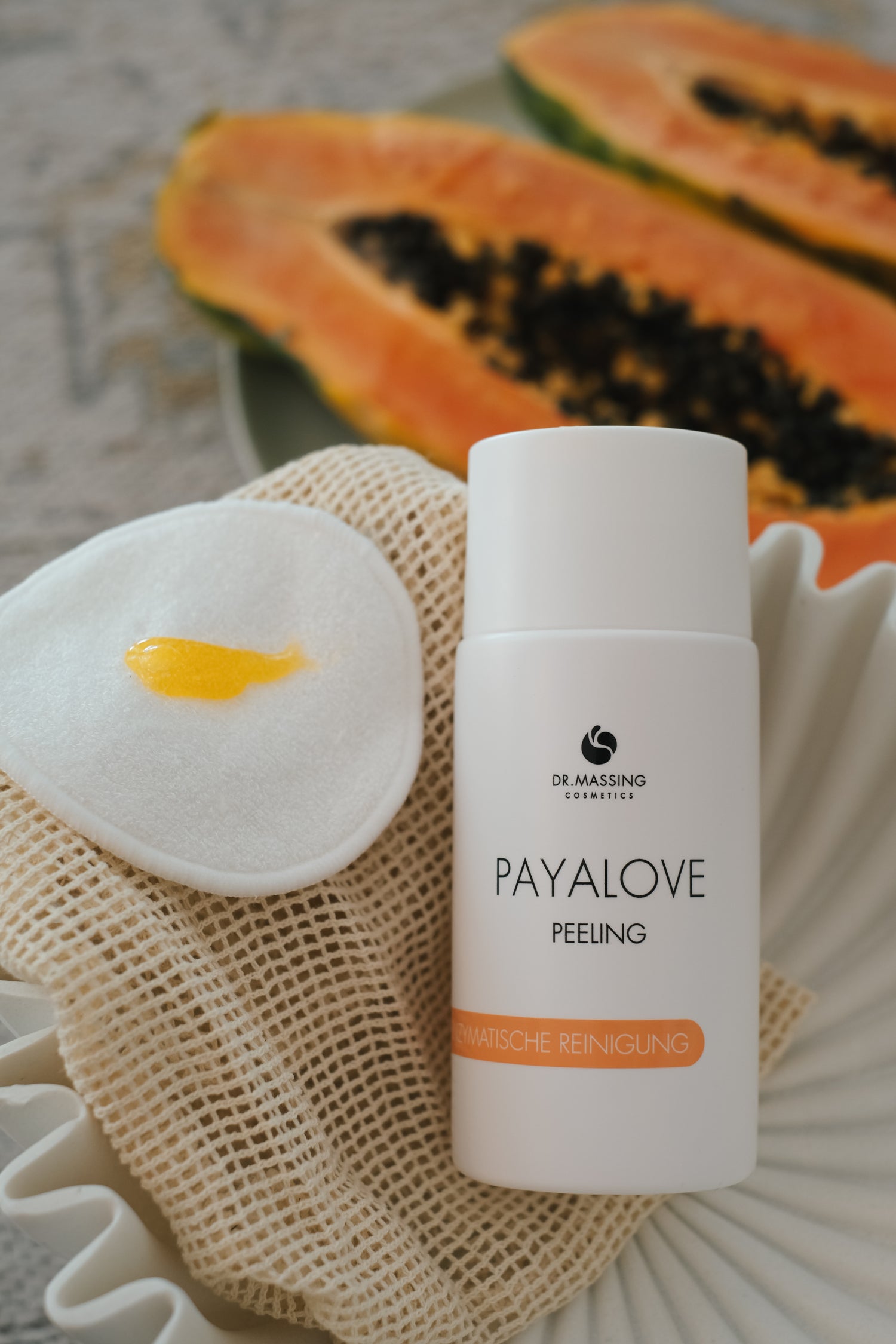 Payalove Peeling liegt in beiger Schale neben Papaya und Wattepad mit Peeling Textur 