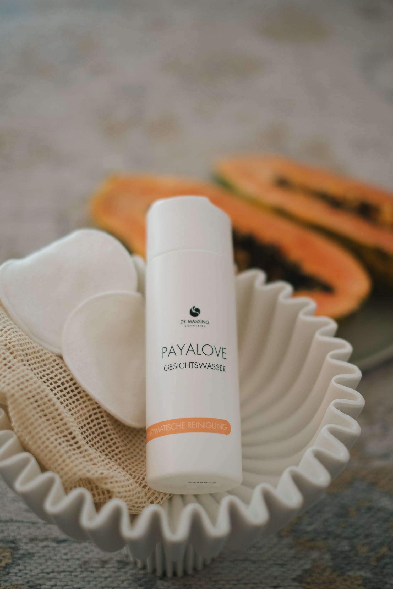 Payalove Gesichtswasser liegt in beiger Schale neben Papaya und Wattepads