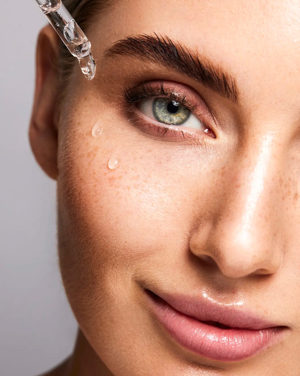 Eine Frau mit strahlender und gepflegter Gesichtshaut trägt das Hyalove 6-fach Hyaluronserum mit der Pipette auf ihre Haut auf und blickt dabei in die Kamera
