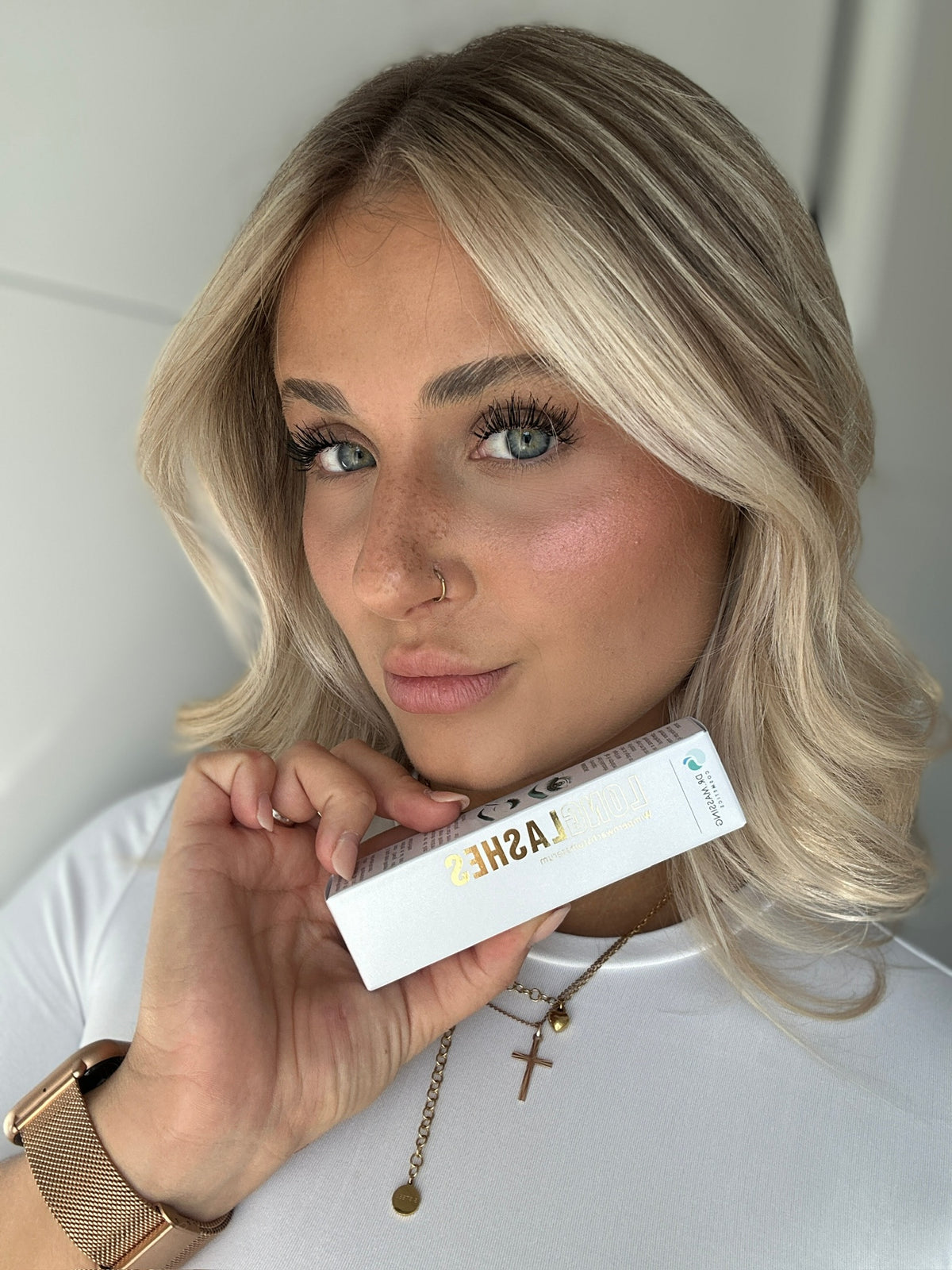 Frau mit langen schwungvollen Wimpern hält Long Lashes Classic Wimpernserum in der Hand und lächelt freundlich in die Kamera