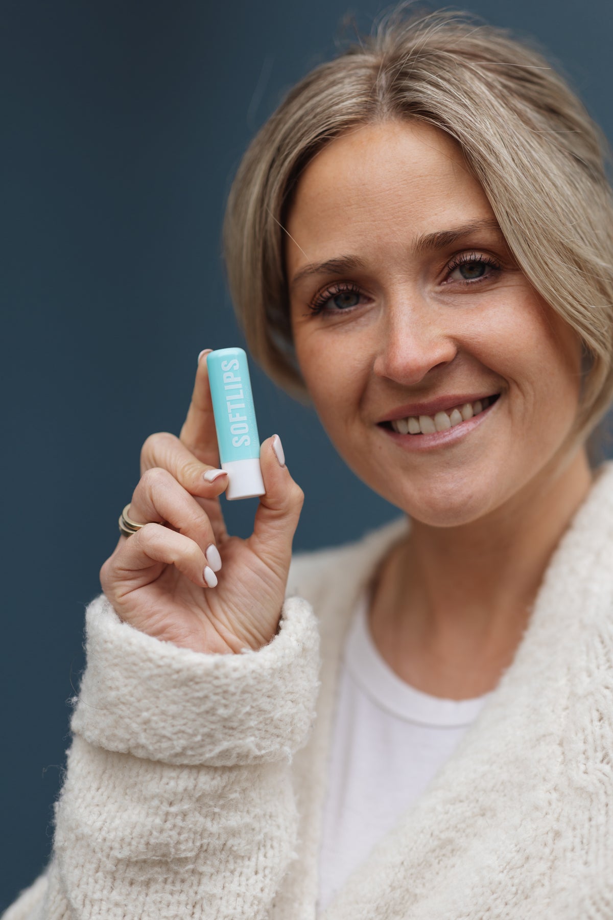 Frau hält Dr. Massing Lippenpflege SoftLips nach Anwendung neben ihr Gesicht und schaut zufrieden in die Kamera