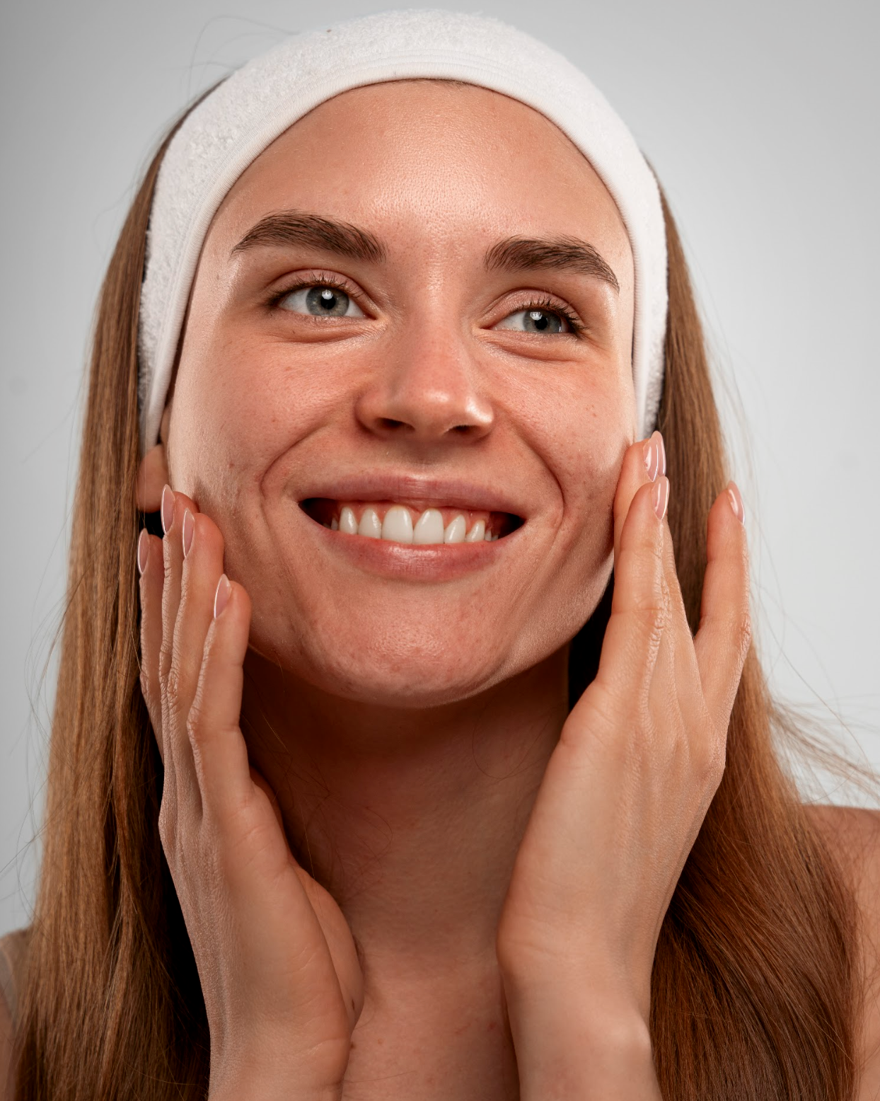 Portrait einer Frau mit Beauty Stirnband und Händen am Gesicht schaut lächelnd in den Spiegel