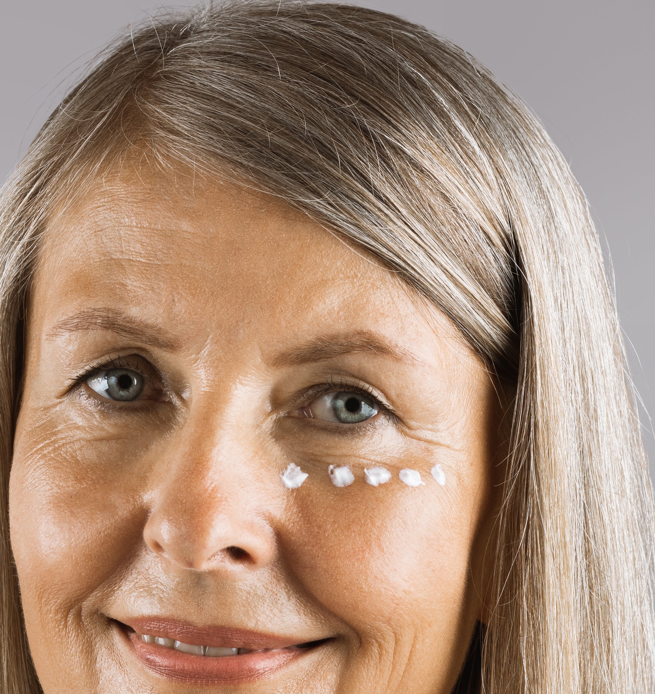 Frau mit reifer Haut und sichtbaren Falten und Schwellungen unter den Augen hat Augencreme unter den Augen aufgetragen