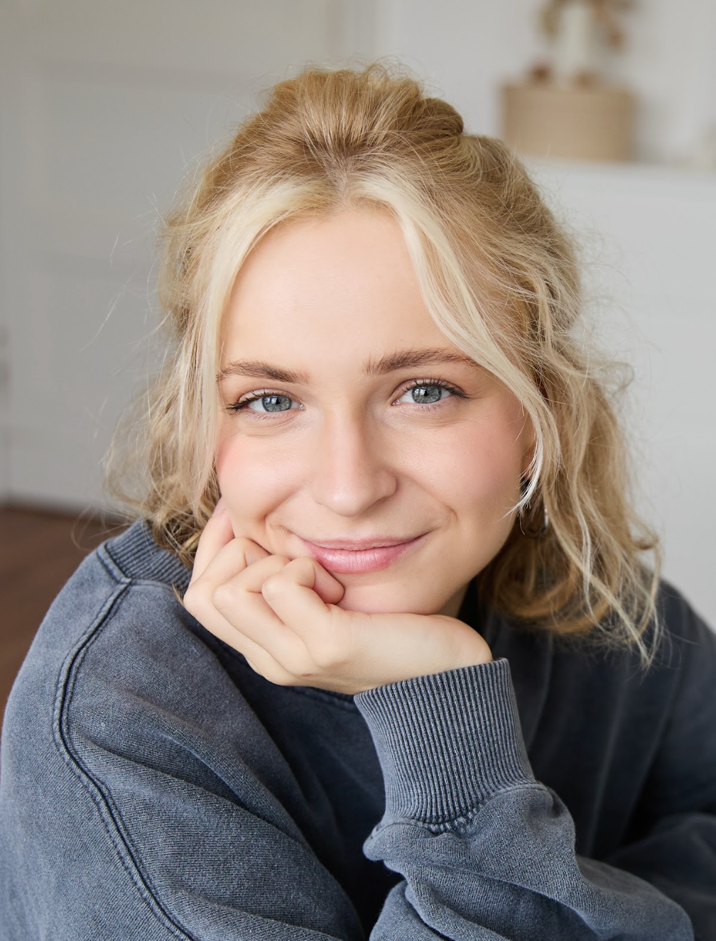 Portrait einer jungen Frau stützt ihr Kinn auf die Handfläche und schaut freundliche in die Kamera