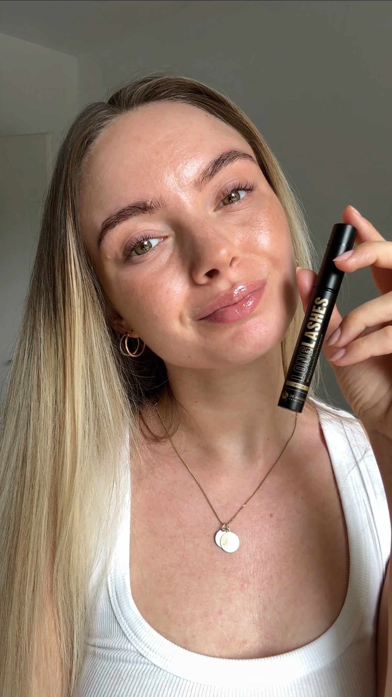 Junge Frau mit schönen vollen Wimpern hält Sensitive Serum neben ihr Gesicht