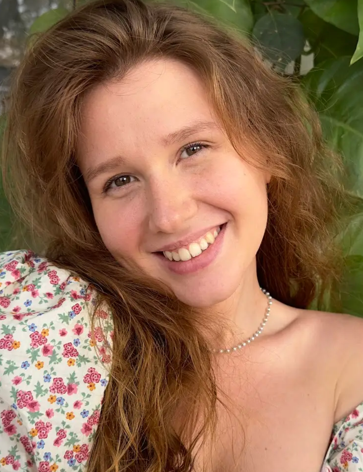 Portrait einer jungen Frau vor einem pflanzlichen Hintergrund lacht freundlich in die Kamera