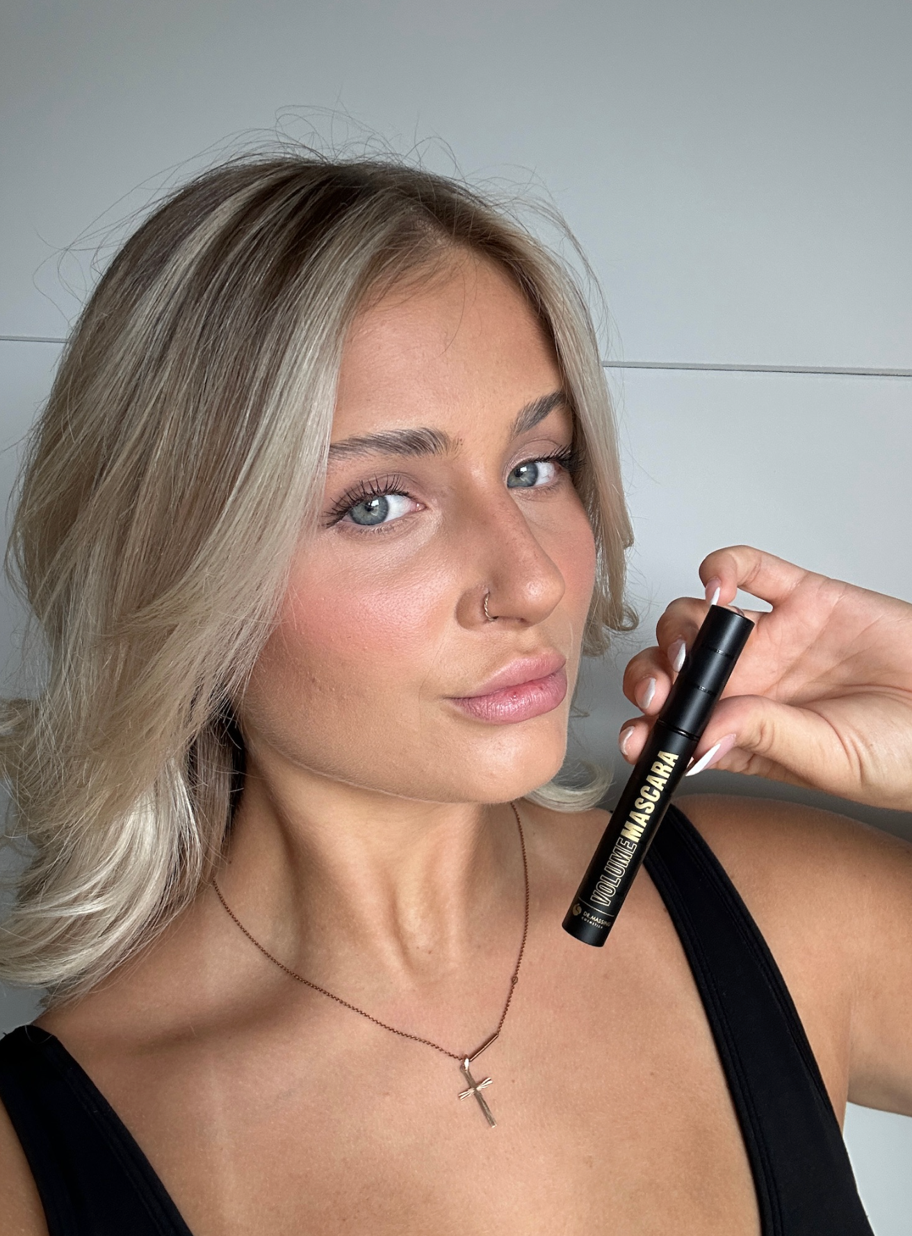 Junge Frau mit schönen vollen Wimpern hält Mascara Produkt neben ihr Gesicht