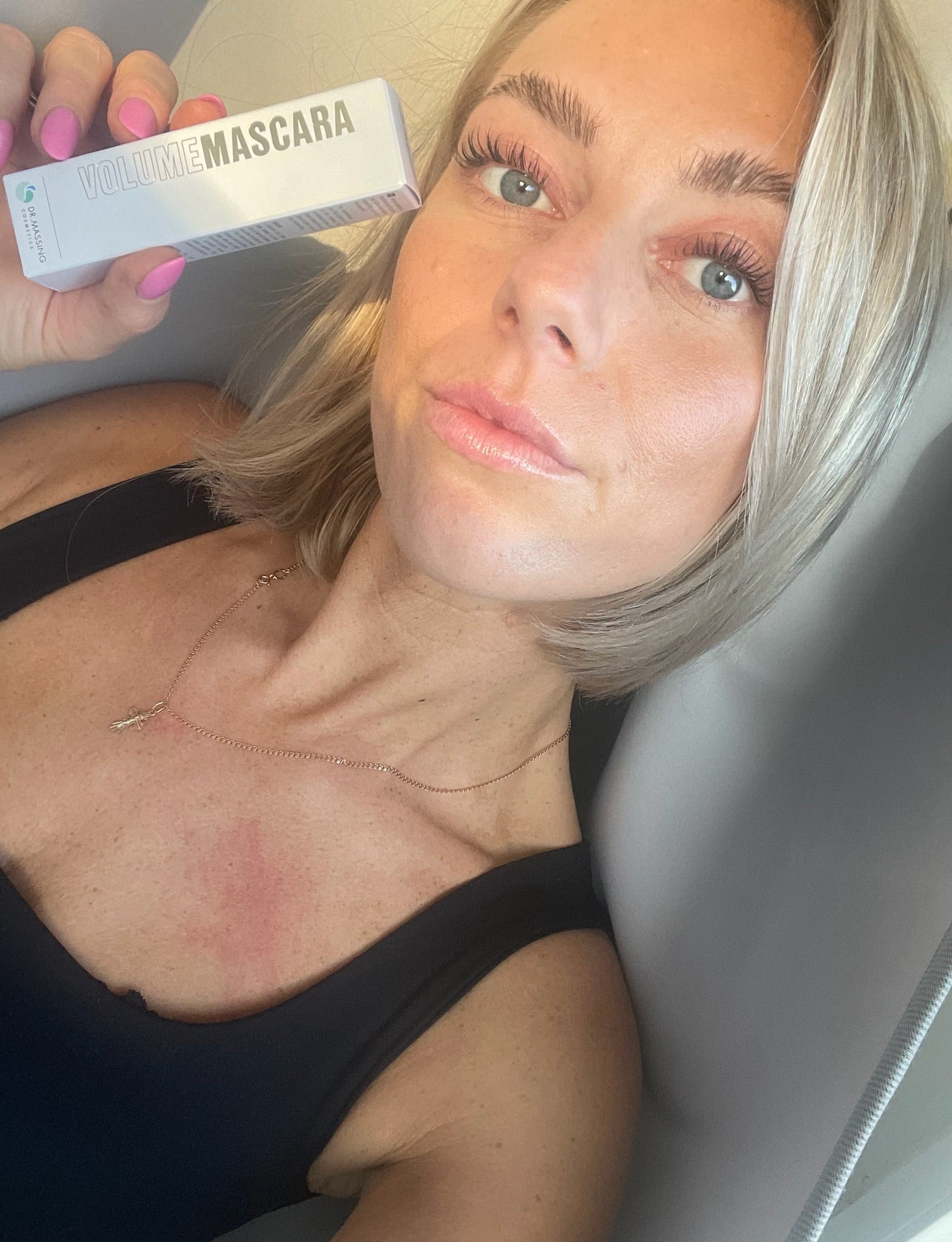 Junge Frau mit schönen Wimpern hält Verpackung der Mascara neben ihr Gesicht
