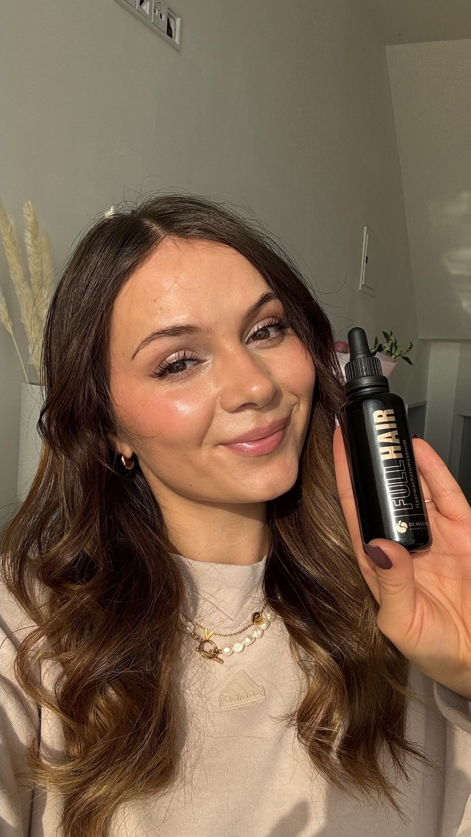 Eine junge Frau hält das Full Hair Serum in die Kamera und lächelt