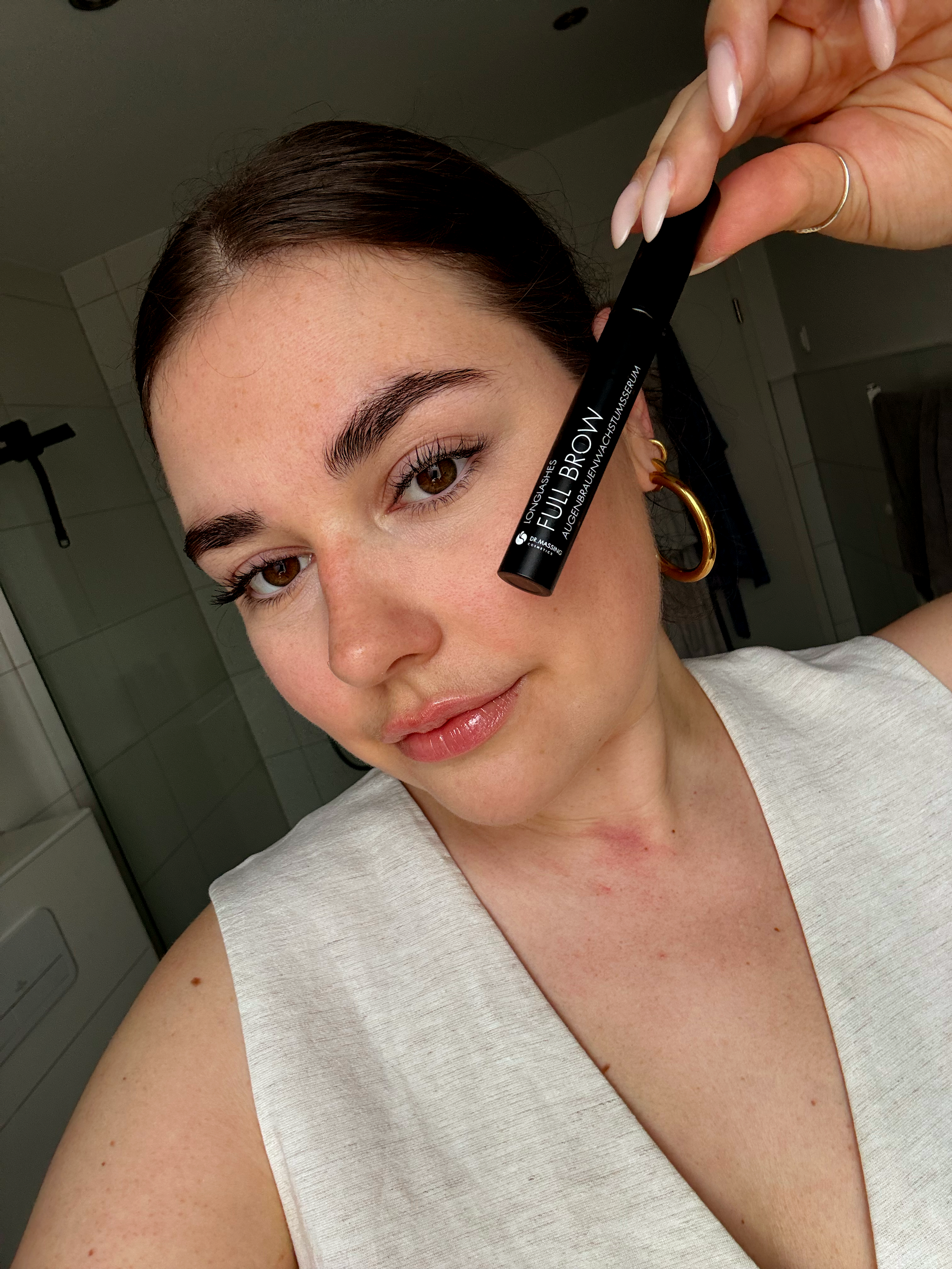 Eine junge Frau hält das Full Brow Augenbrauenserum in die Kamera