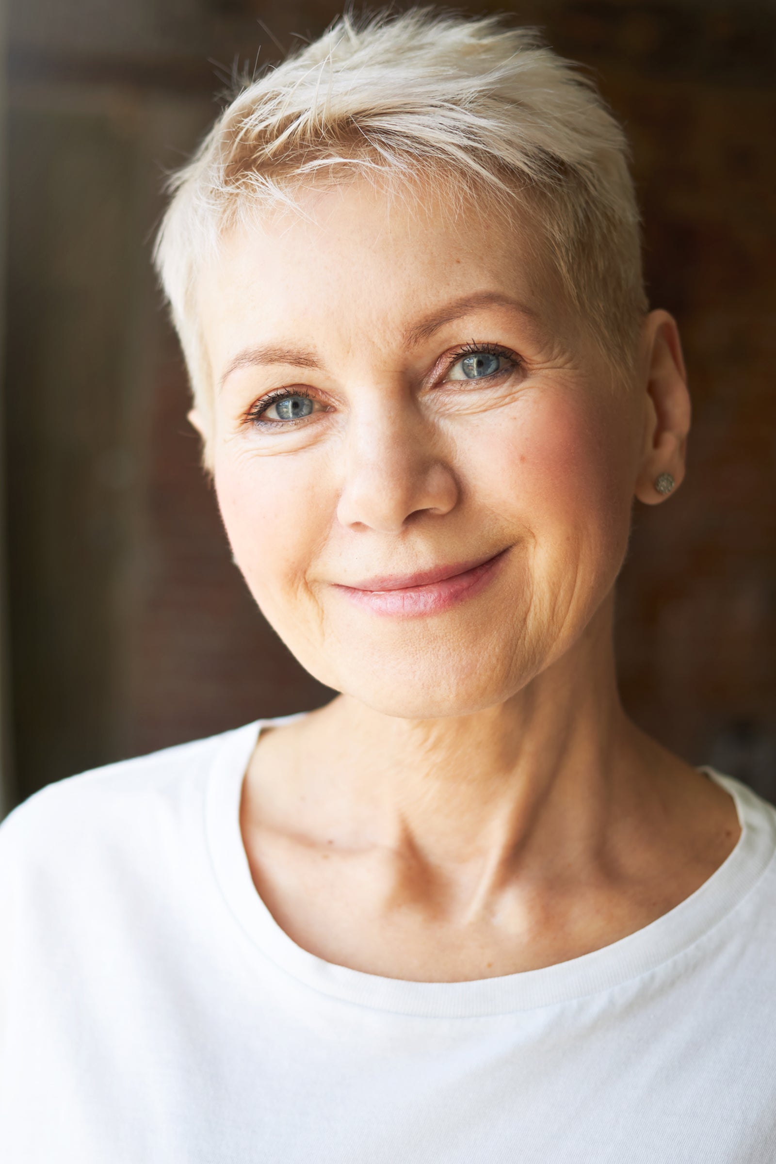Portrait einer blonden Frau mit kurzen Haaren und gepflegter Gesichtshaut und ersten Anzeichen von Hautalterung.