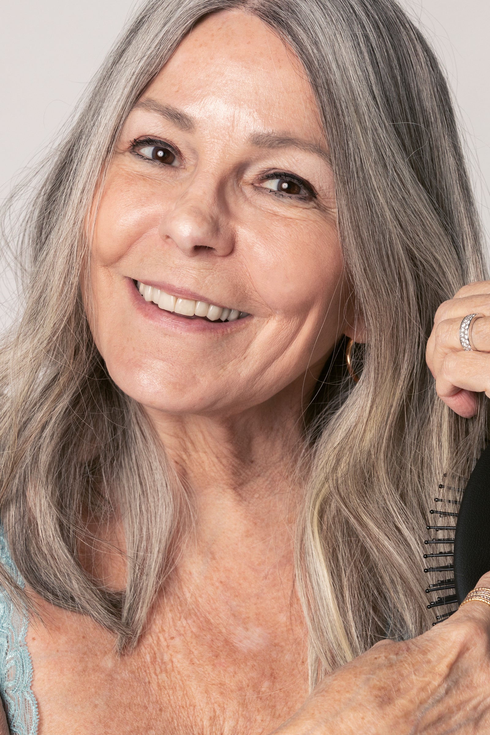 Portrait einer älteren Frau mit gepflegten Haaren, die sich durch die grauen Haare bürstet. 