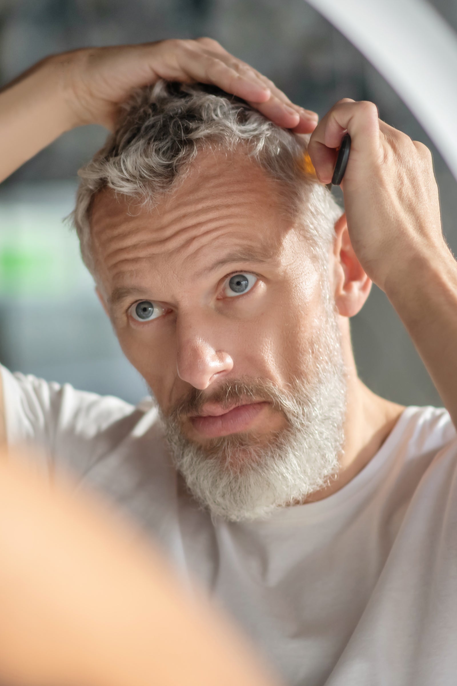 Portrait eines älteren Mannes mit gepflegten Haaren, der sich durch die grauen Haare kämmt. 