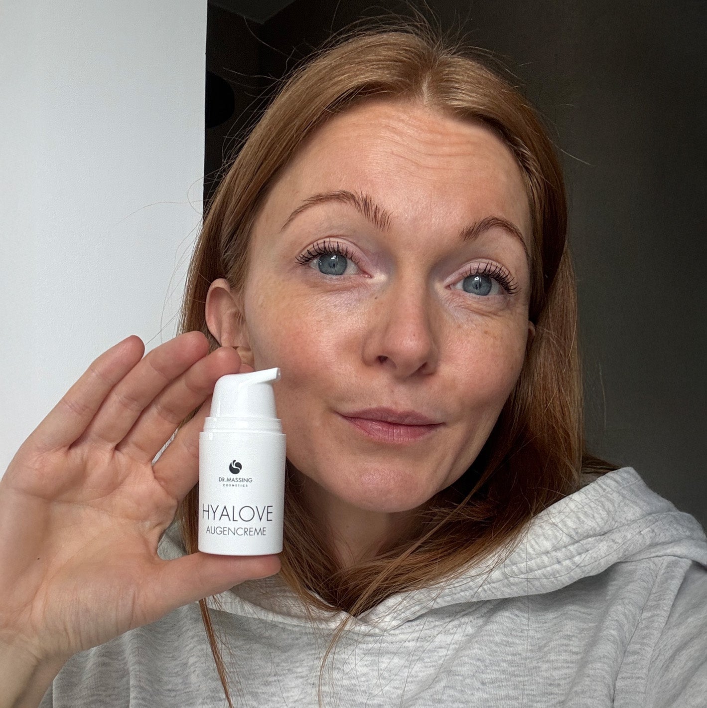 Nahaufnahme einer Frau welche die Hyalove Augencreme neben ihrem Gesicht in der Hand hält.