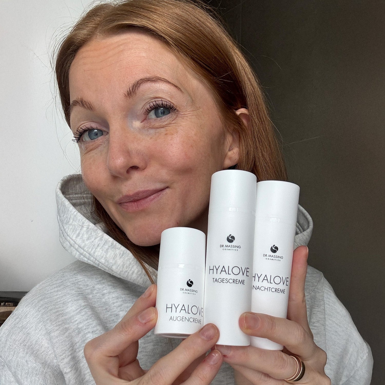 Nahaufnahme einer Frau welche die Hyalove Creme Kollektion (Augencreme, Tagescreme und Nachtcreme) neben ihrem Gesicht in der Hand hält.