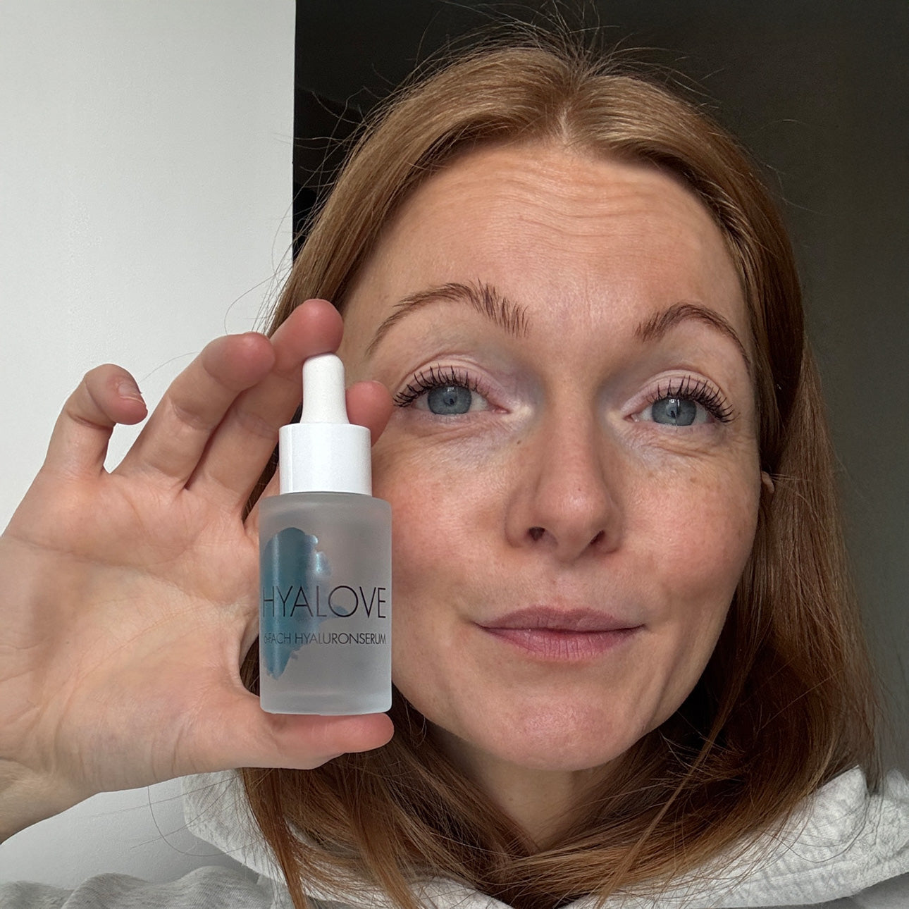 Nahaufnahme einer Frau welche das Hyalove Hyaluronserum neben ihrem Gesicht in der Hand hält.