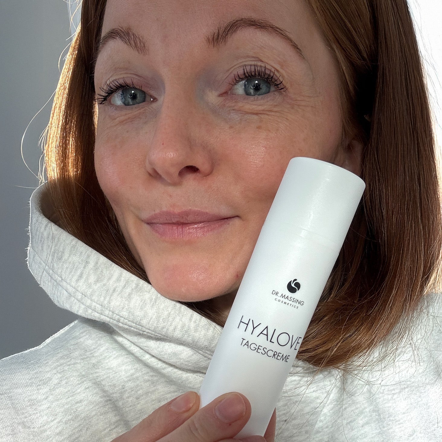 Nahaufnahme einer Frau welche die Hyalove Tagescreme neben ihrem Gesicht in der Hand hält.