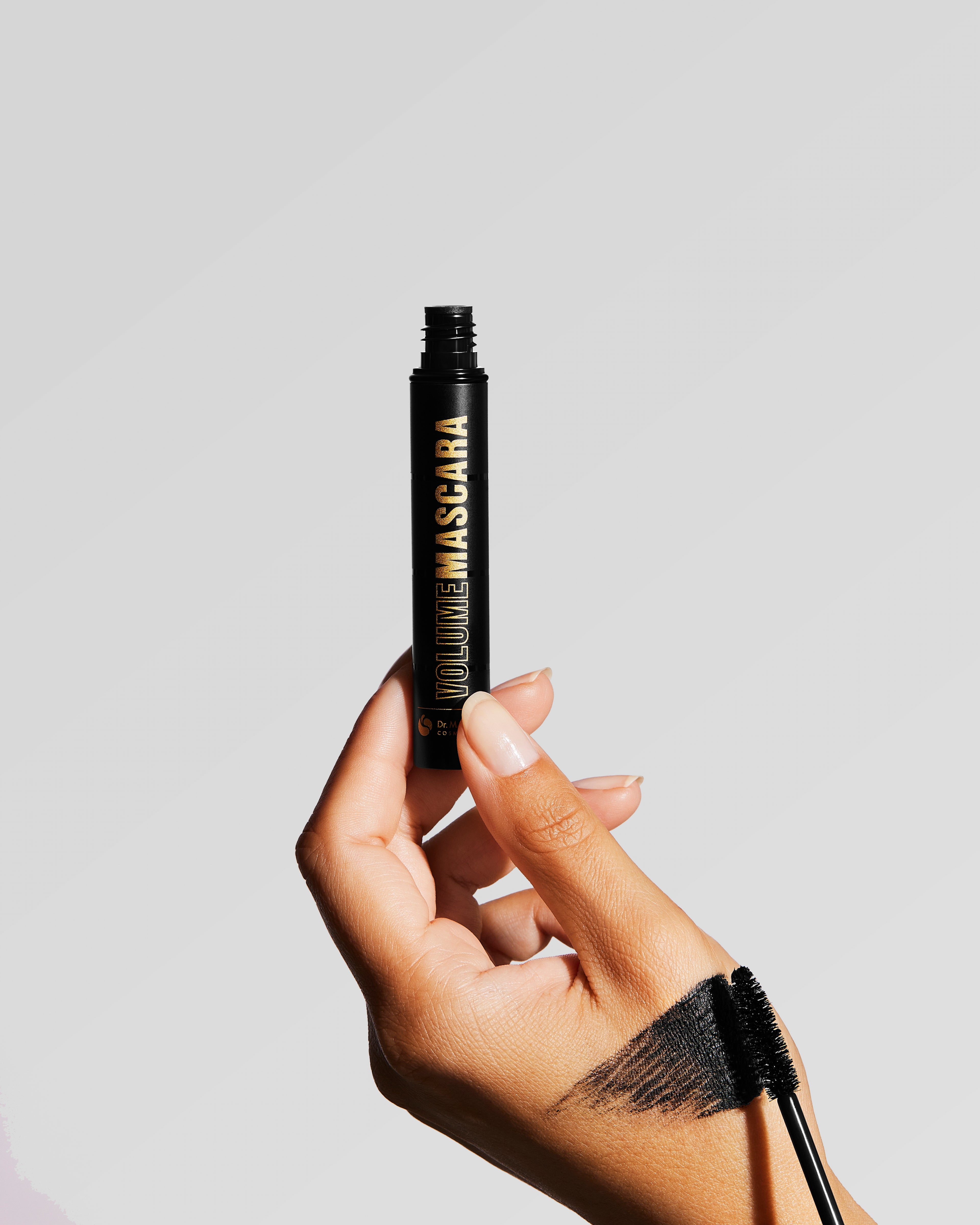 Eine Hand hält die Volume Mascara, die andere Hand streicht mit der Bürste über den Handrücken